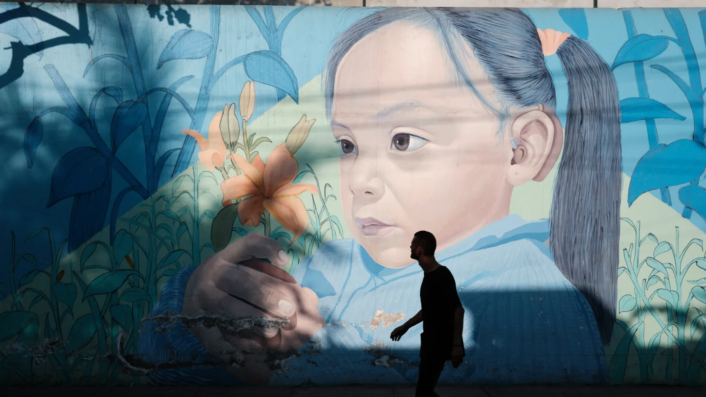 Silhouette of a man walking past a large mural of a young girl holding a flower