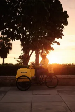 Drinks vendor sitting on bicycle as sun sets behind