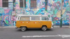 Yellow VW Campervan parked in front of wall covered in Graffiti