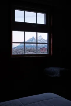 A window can be seen from inside a cabin, the view through the window shows snowy mountains in Torres del Paine, Chile.