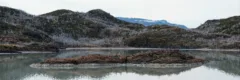 A still body of water, surrounded by grey hills in Torres del Paine National Park, Chile.