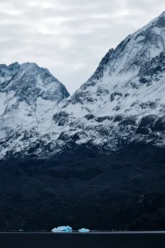 A small iceberg floats past snow-capped mountains in Lago Grey, Torres del Paine National Park, Chile.