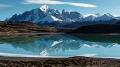 A turquoise lake, backed by snow-capped mountains in Torres del Paine National Park, Chile. A perfect reflection of the mountains is mirrored in the lake.