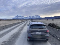 A black car driving on a long straight road, towards snow-capped mountains in Torres del Paine National Park, Chile.