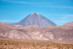 Dusty hillsides and a volcano are backed by a bright blue sky in the Atacama Desert.