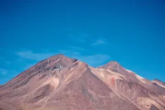 Red, dusty mountain peaks are backed by a bright blue sky.