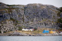 Colourful wooden houses sit on the oceans edge at the base of rocky cliffs.