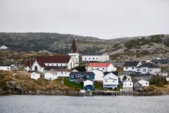 White wooden houses and a white church on a rocky patch of land that leads to the ocean.