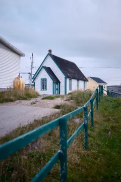 A white wooden house with a green wooden fence outside.