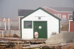 A white wooden building with green trim. A fishing buoy hangs from the door.