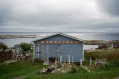 A blue wooden shed sits backed by the ocean. A sign above the door reads S.Blandford.