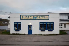 White building with blue windows and doors. A sign reads This & That Store above the door.