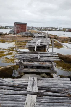 Small red wooden building and a collapsed wooden bridge leading to it in Tilting, Fogo.