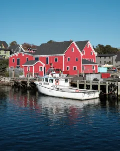 A large red wooden building sits behind a small white boat that is tied up.