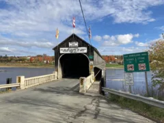 A covered bridge crosses a river. A sign claims it is the world's longest covered bridge.