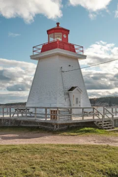 A white lighthouse with a red roof sits on a grassy patch of land.