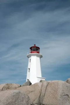 A white lighthouse with a red roof stands on some rocks.