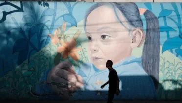 Silhouette of a man walking past a large mural of a young girl holding a flower