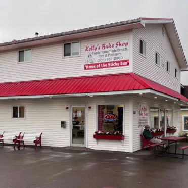 A large white building with a red roof. The sign on the side reads "Kelly's Bakery". There is an open sign in the window.