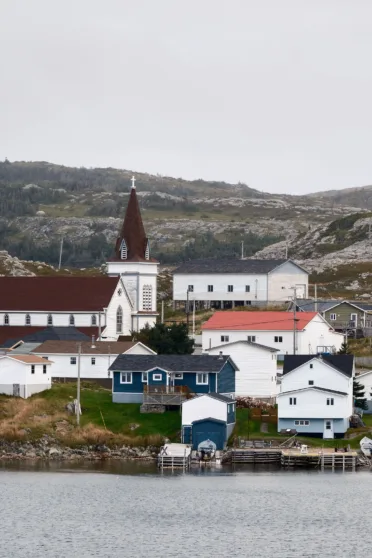 White wooden houses and a white church on a rocky patch of land that leads to the ocean.