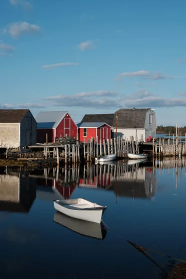 Small fishing boats are docked at a harbour with colourful wooden buildings.