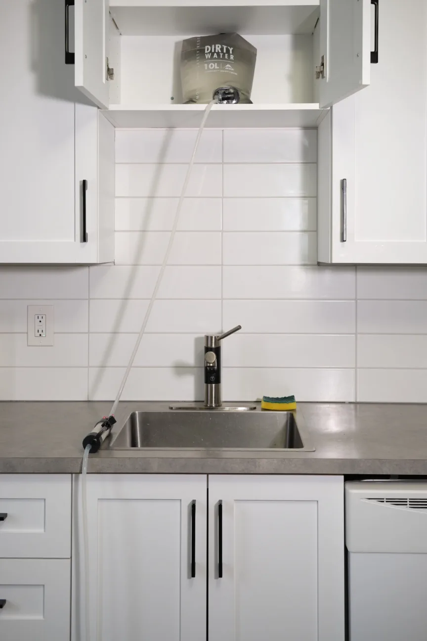 An MSR Guardian Gravity Purifier sitting in a white cupboard, filtering water in a white tiled kitchen.