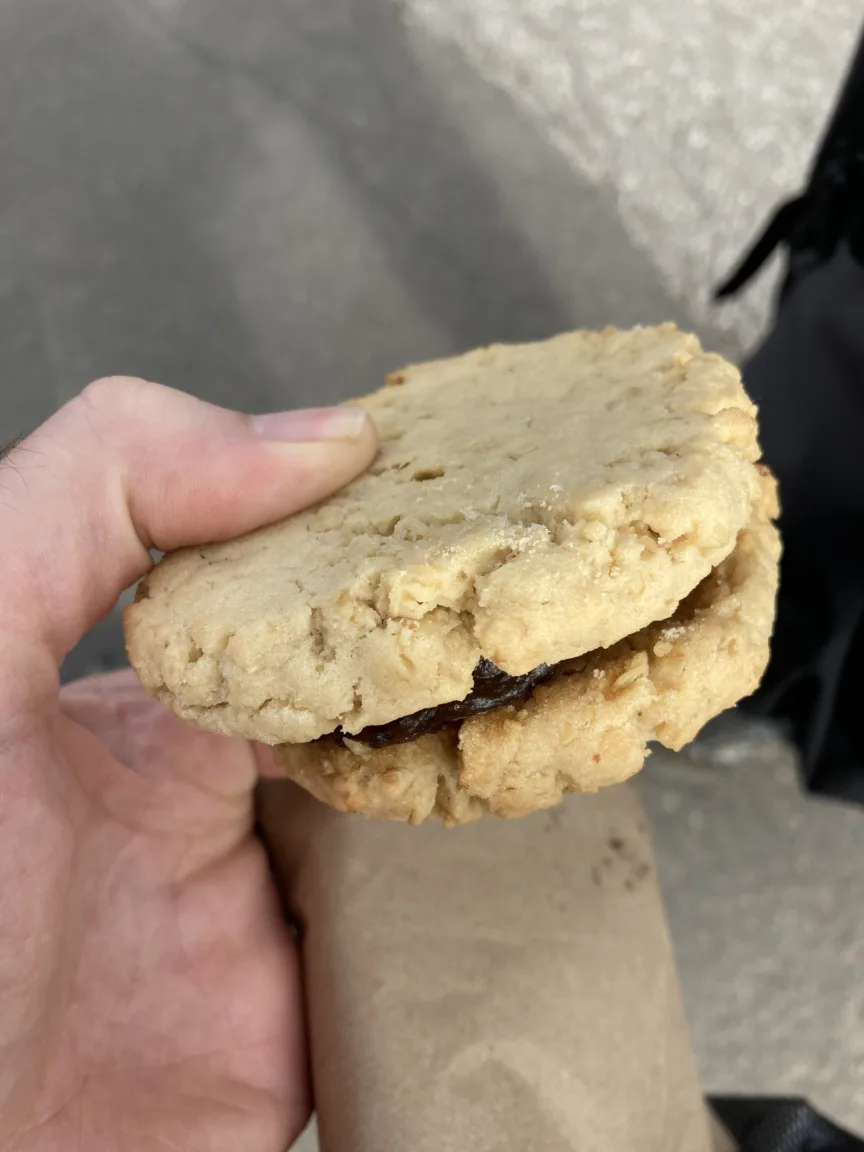 A hand holding two coconut cookies sandwiched together with a sticky date filling.