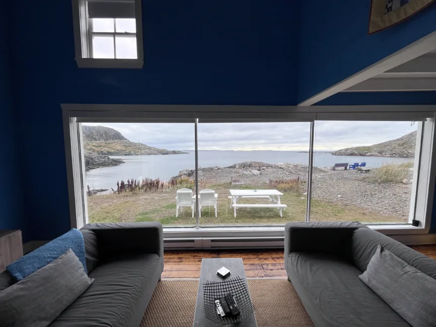 A living room with a large picture window. Views of a small bay can be seen.