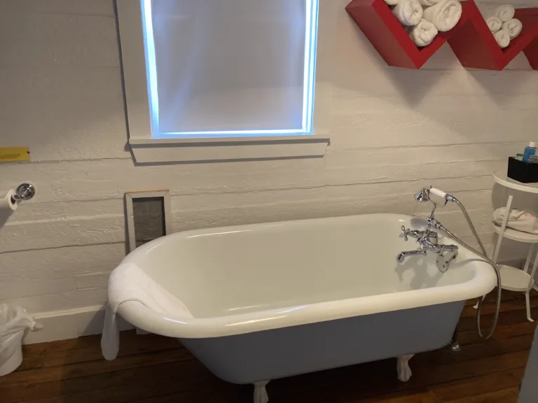 A claw foot bathtub stands in a white bathroom with wooden flooring.