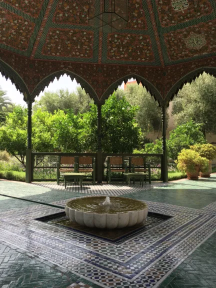 A shallow fountain is surrounded by blue and green Moroccan floor tiles. It is covered by a patterned gazebo.