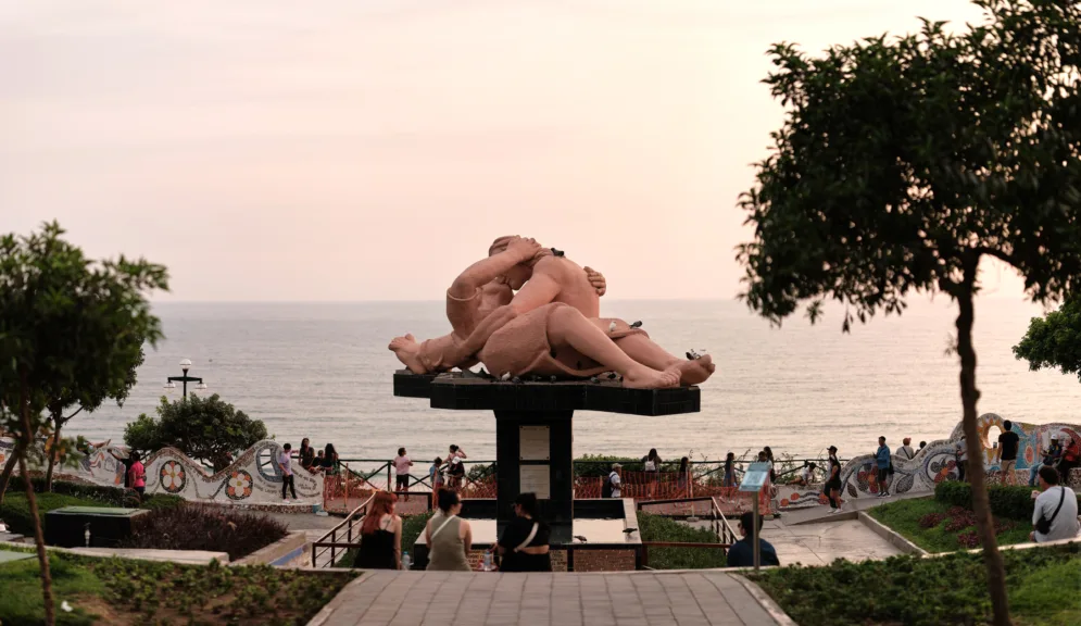 A famous kissing sculpture in a park by the ocean.