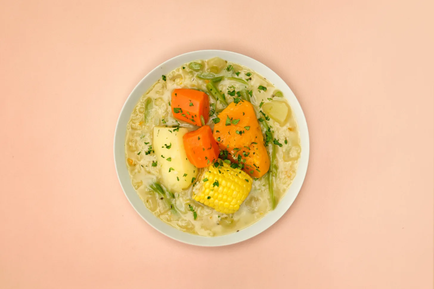 A bowl of Chilean vegetable stew on a pink background.