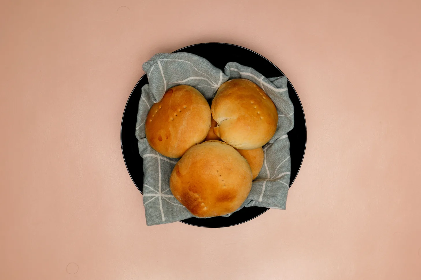 A black bowl full of freshly baked bread rolls.