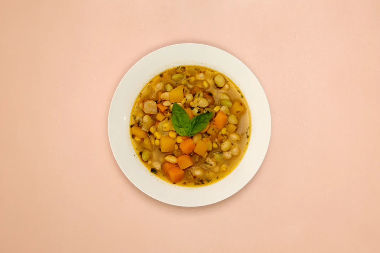 A white bowl full of Porotos Granados, a Chilean bean stew. It sits on a pink background.