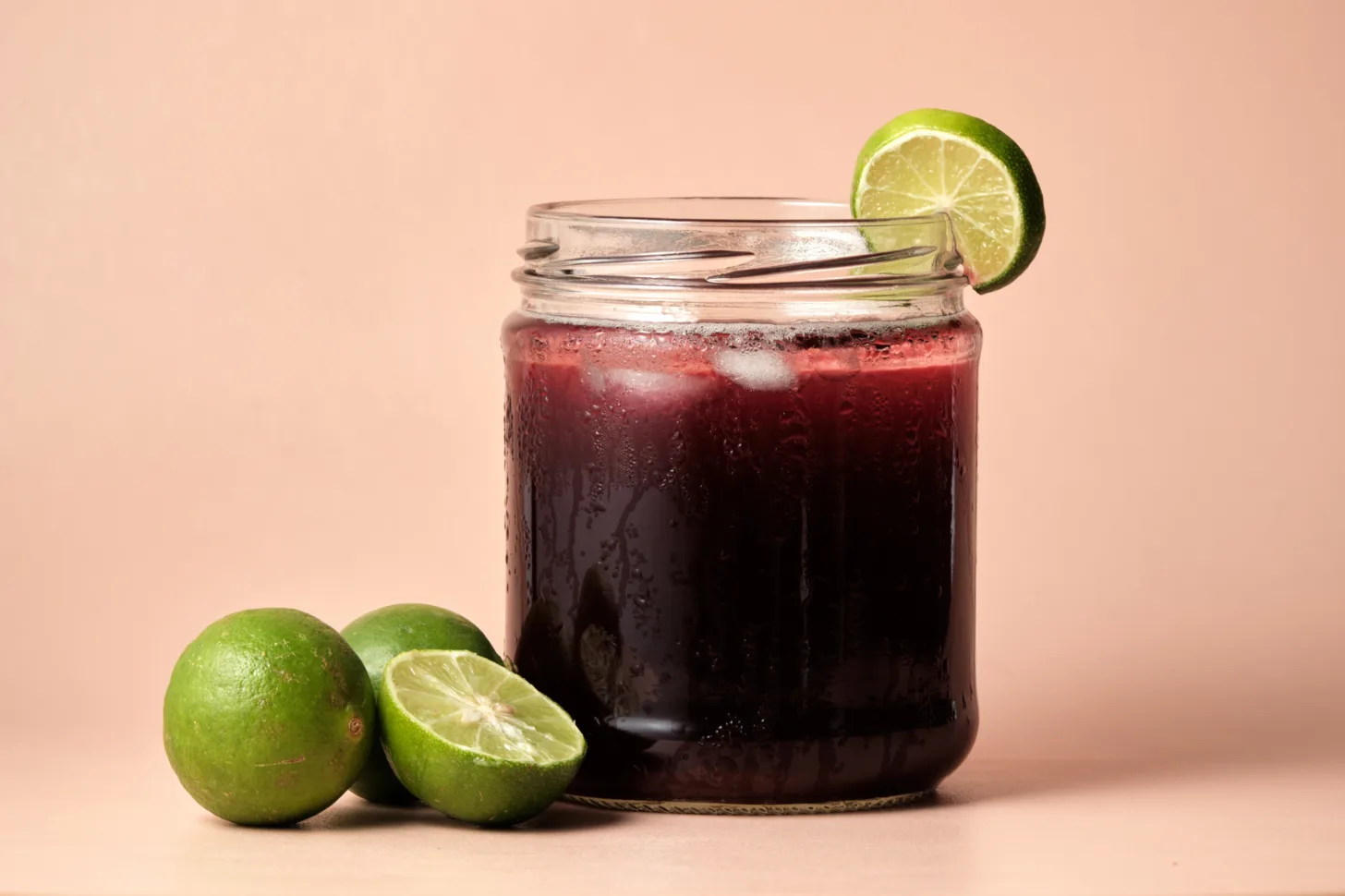 Chicha Morada in a glass jar with limes placed next to it.