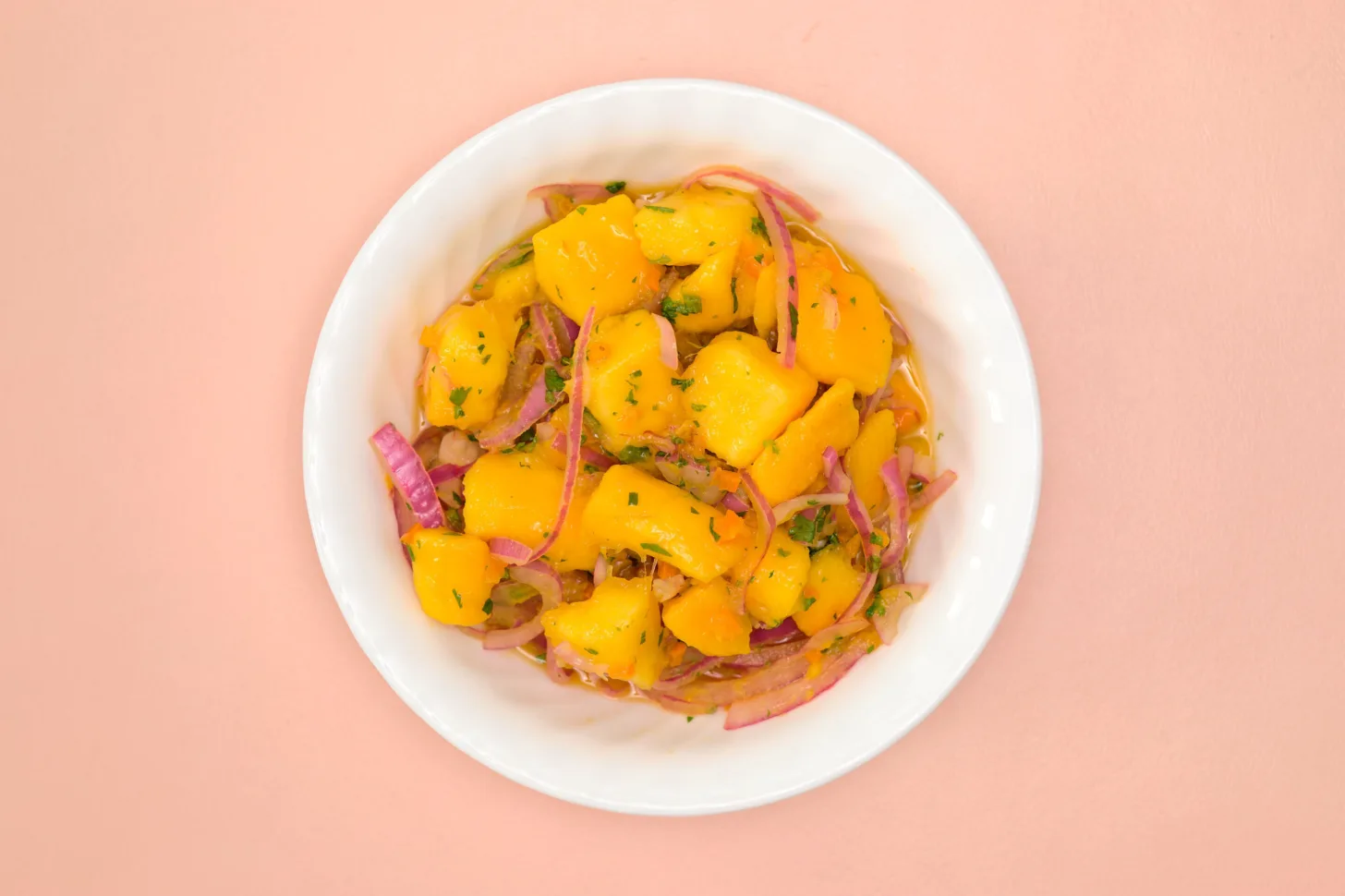 An overhead view of a white bowl filled with Mango Ceviche on a pink background.