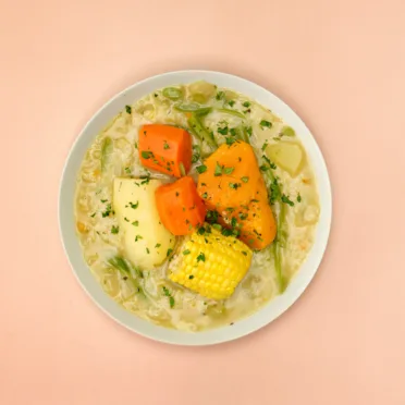 A bowl of Chilean vegetable stew on a pink background.