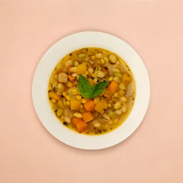 A white bowl full of Porotos Granados, a Chilean bean stew. It sits on a pink background.