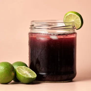 Chicha Morada in a glass jar with limes placed next to it.