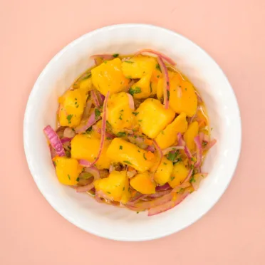 An overhead view of a white bowl filled with Mango Ceviche on a pink background.