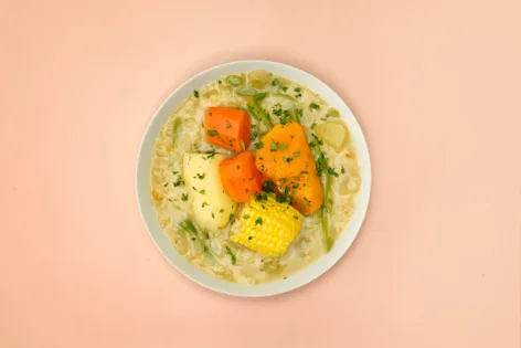 A bowl of Chilean vegetable stew on a pink background.