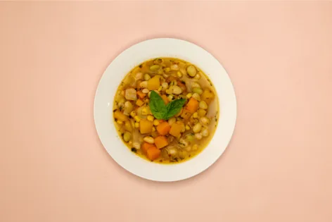 A white bowl full of Porotos Granados, a Chilean bean stew. It sits on a pink background.