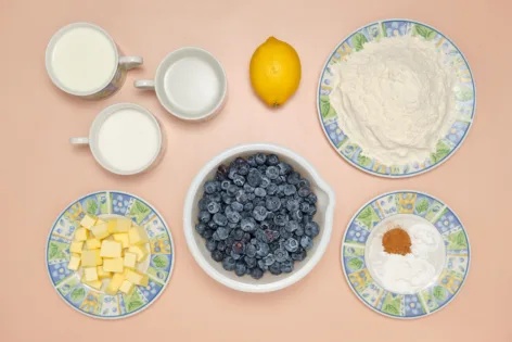 The ingredients needed to make a blueberry grunt are arranged on a pink background.