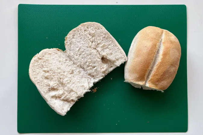 Two bread rolls on a green chopping board. One is sliced in halve.