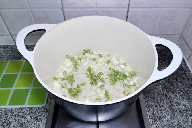 A large pan with onions and celery frying in it.