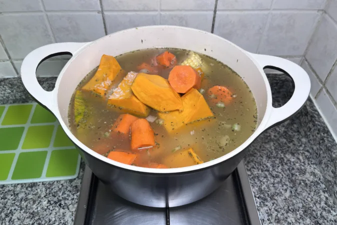 A pot of Chilean vegetable stew with corn, squash, carrot and potatoes being added to it.