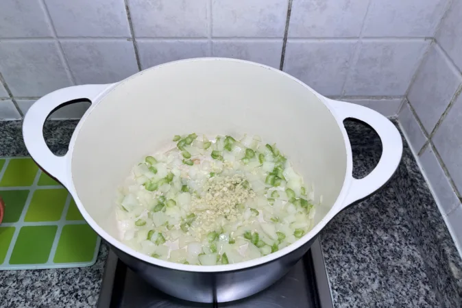 A large saucepan with onion, celery and garlic frying in it.