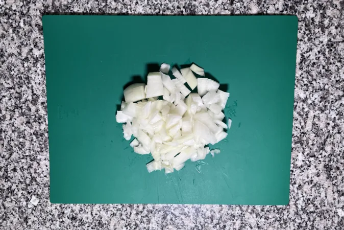 A chopped onion on a green chopping board.