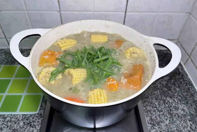 A pot of Chilean vegetable stew with green beans being added.