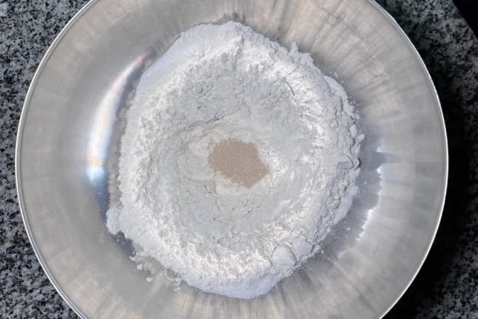 A silver bowl full of flour, yeast and salt.